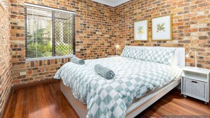 A bedroom with a brick wall, a bed with checkered bedding, a bedside table with a lamp, and two framed pictures on the wall. - 57Charlton - Luxury Beach House - secluded area of Nambucca, 5 minute walk to the beach (Nambucca Heads)