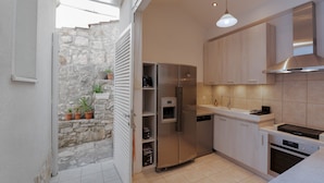 Una cocina compacta con refrigerador, horno y lavavajillas integrados. Cuenta con muebles de tono claro y una pared de piedra en el exterior.