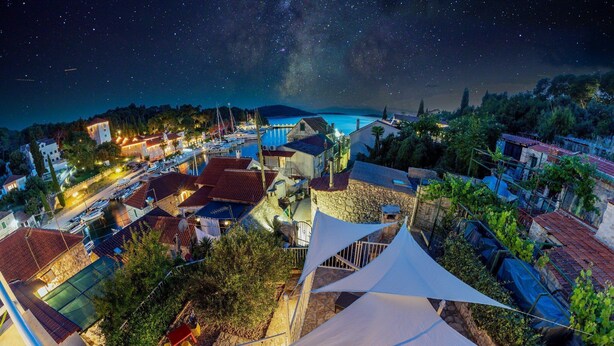 Un pueblo costero de noche con un puerto deportivo, edificios de piedra y una vista despejada de las estrellas.