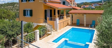 A two-story house with a swimming pool, a balcony, and a view of the surrounding landscape.