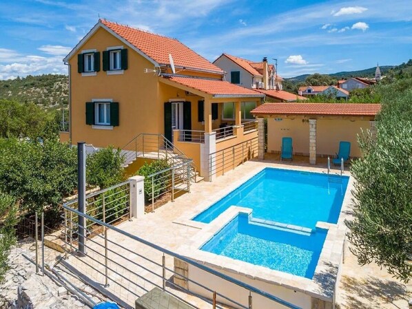 A two-story house with a swimming pool, a balcony, and a view of the surrounding landscape.