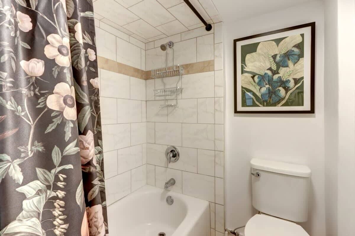 Une salle de bain équipée d’une baignoire, d’une douche, de toilettes et ornée d’une œuvre d’art florale encadrée au mur.