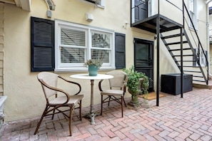 An outdoor patio with two wicker chairs and a small round table, a potted plant, and a black speaker.