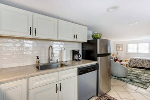 A modern kitchen with white cabinets, a stainless steel refrigerator, a coffee maker, and a dishwasher.
