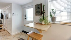 Una cocina con mesa de madera, un banco, una planta en maceta y una ventana con persianas.