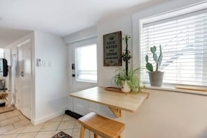 A modern kitchen with a wooden table and bench, a potted plant, and a window with blinds.