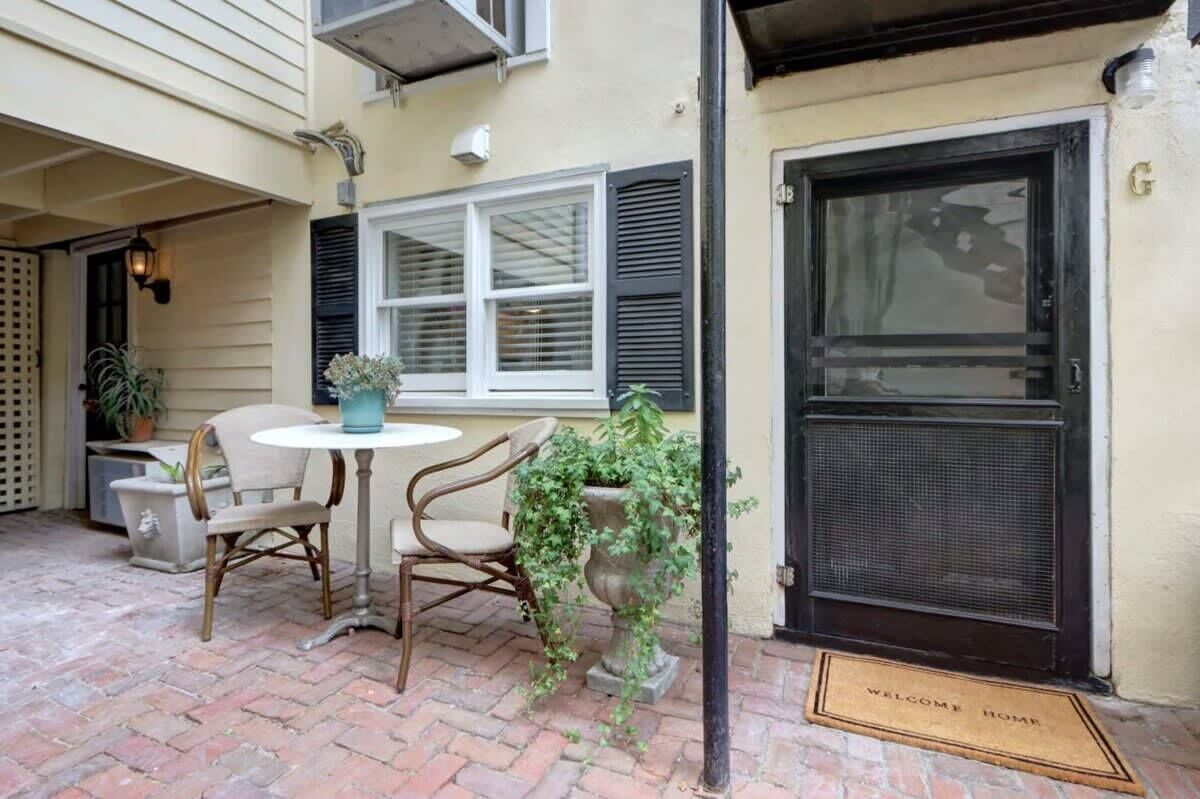 Un patio con una mesa redonda y dos sillas, una planta en maceta y una puerta con felpudo.