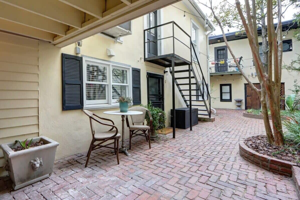 A brick patio with a table and chairs, a small planter, and a black spiral staircase.