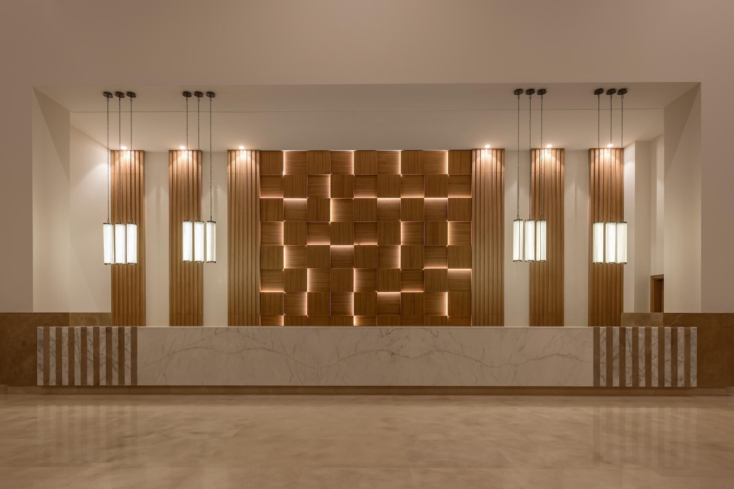 Un mostrador de recepción con pared de paneles de madera, iluminación colgante y suelo de mármol.