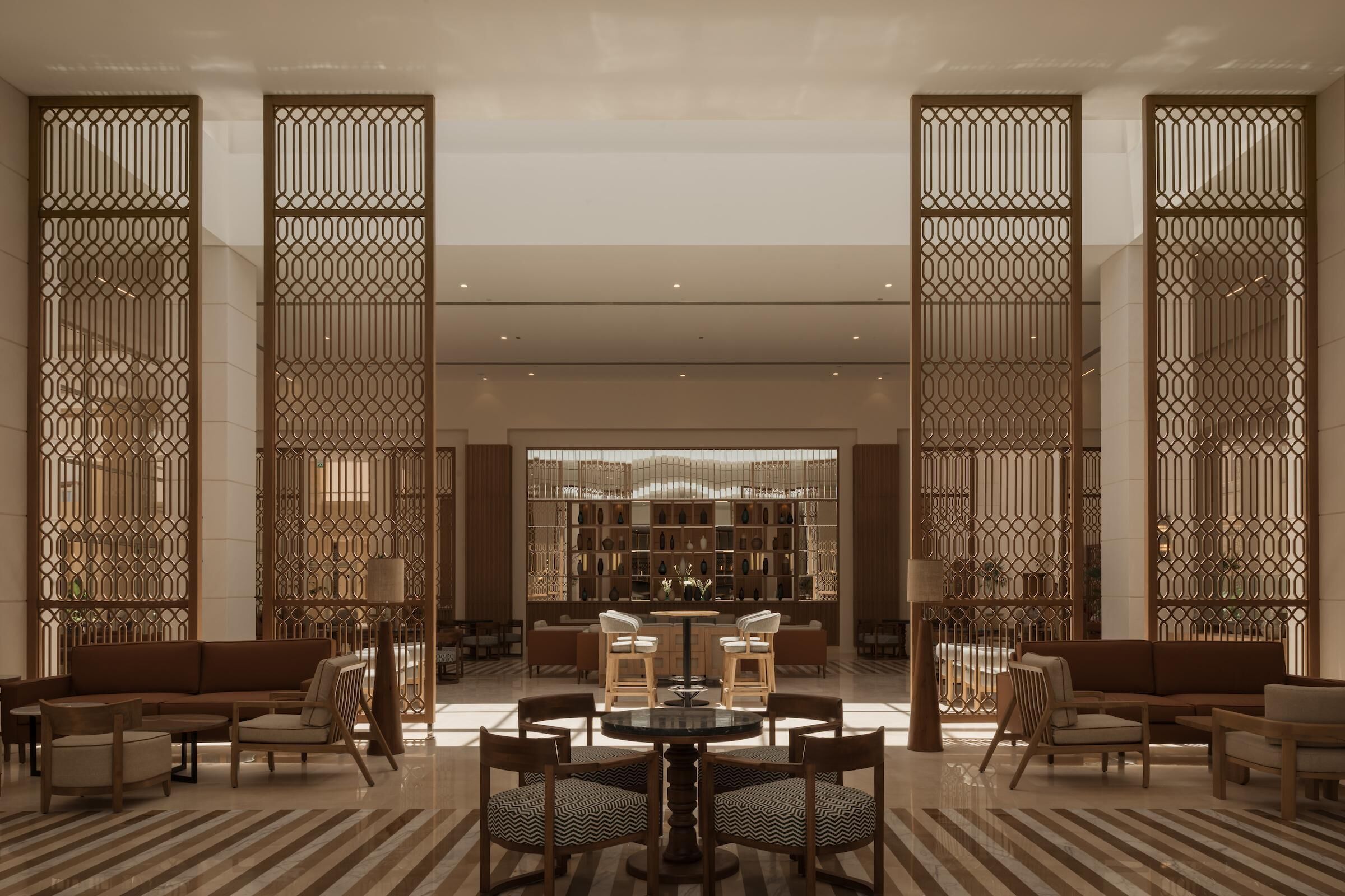A spacious lobby with a central round table surrounded by chairs, sofas, and a decorative wall with a patterned design.