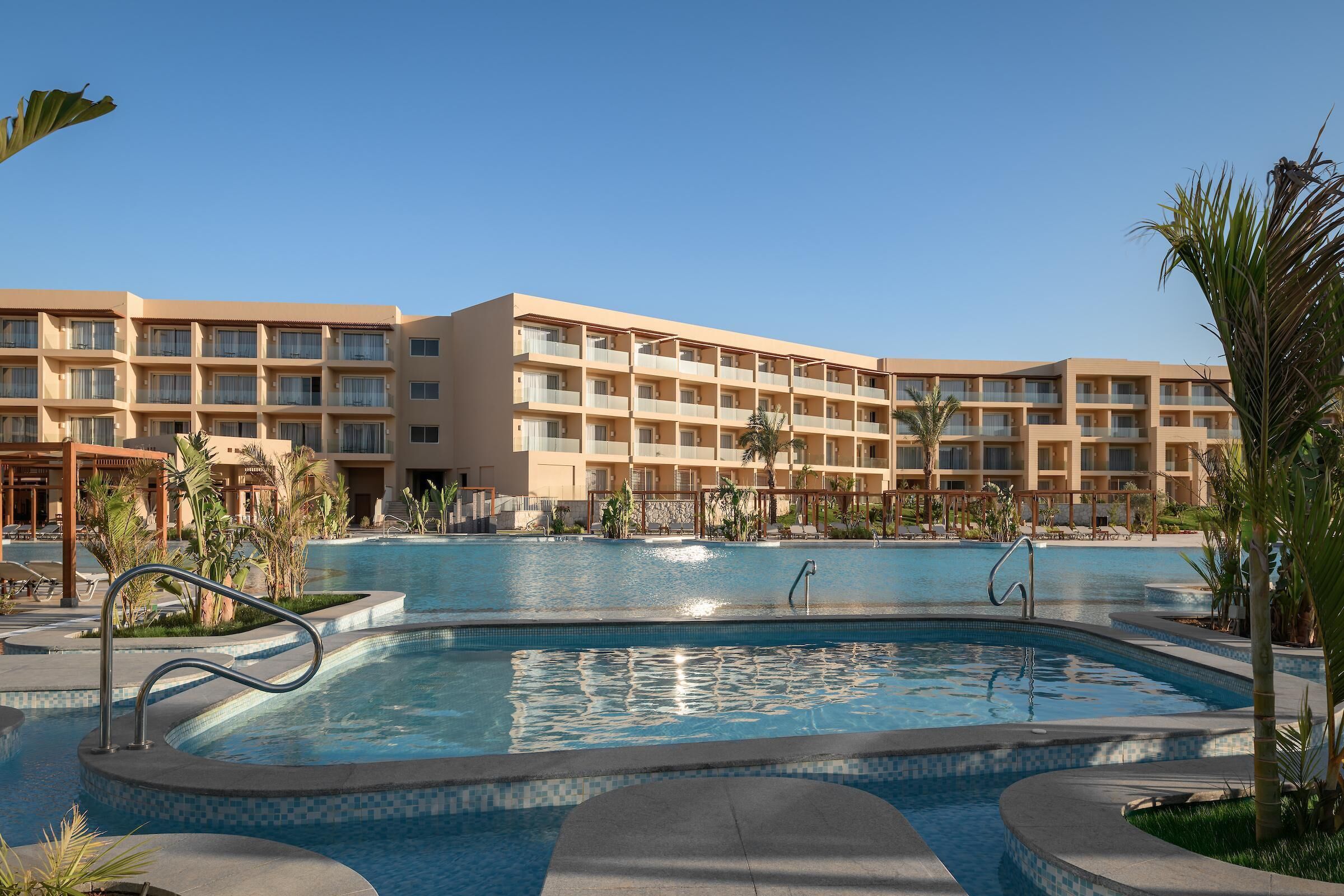 A hotel with a swimming pool, multiple balconies, and palm trees.