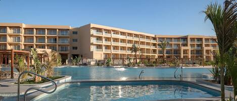 A hotel with a swimming pool, multiple balconies, and palm trees.