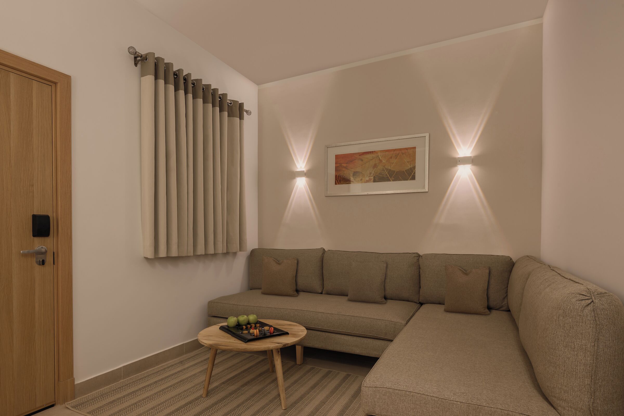 Una sala de estar moderna con un sofá color beige, una pequeña mesa redonda y una puerta con picaporte.