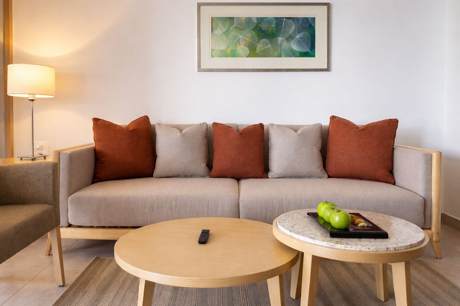 Uma sala de estar com um sofá, uma mesa de centro redonda, um controle remoto e um quadro abstrato emoldurado na parede.