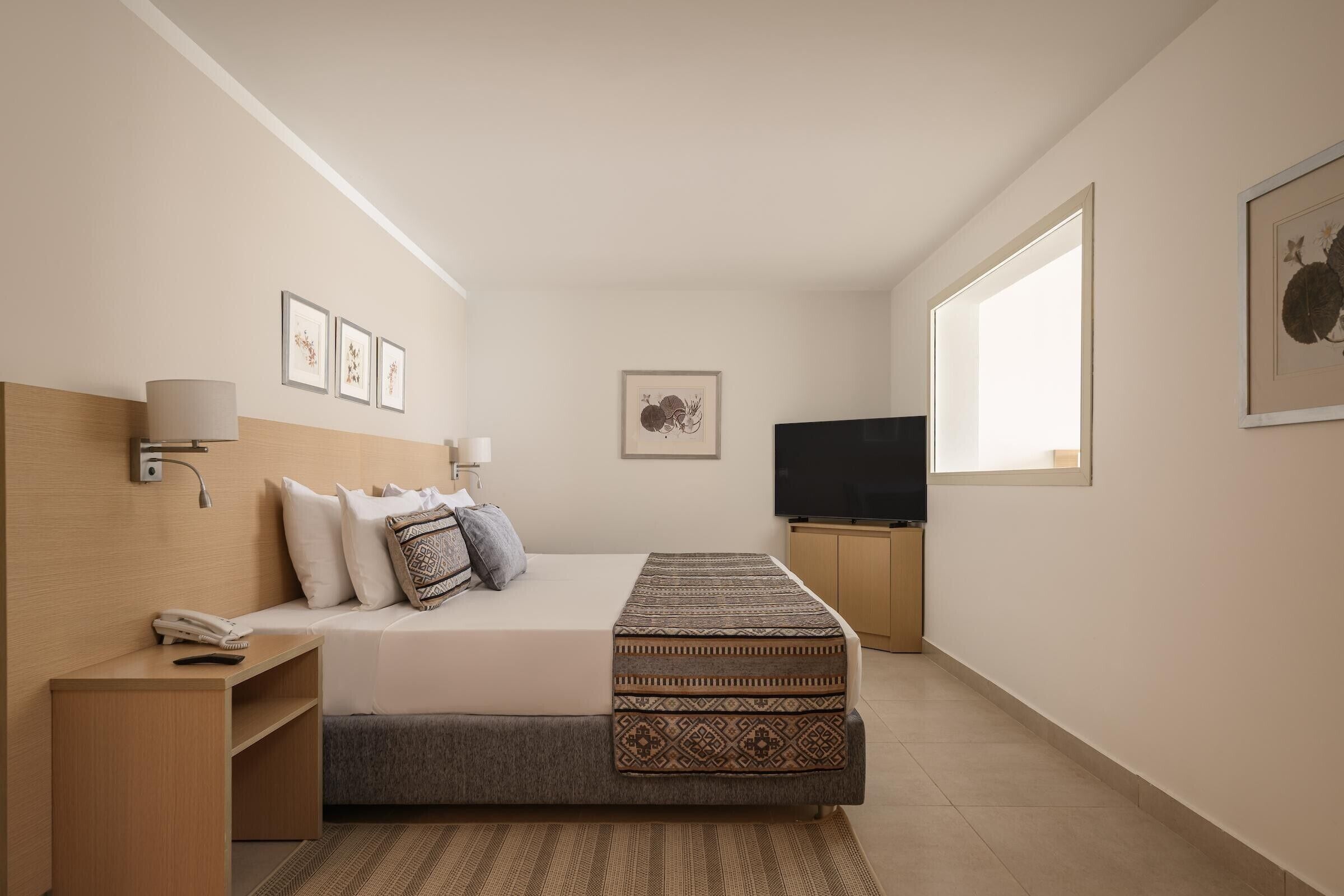 A modern bedroom with a bed, bedside lamps, a TV, and artwork on the walls.