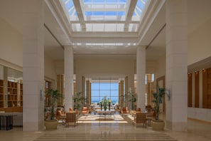 Un lobby espacioso con un área de estar central, ventanas amplias y vista al océano.