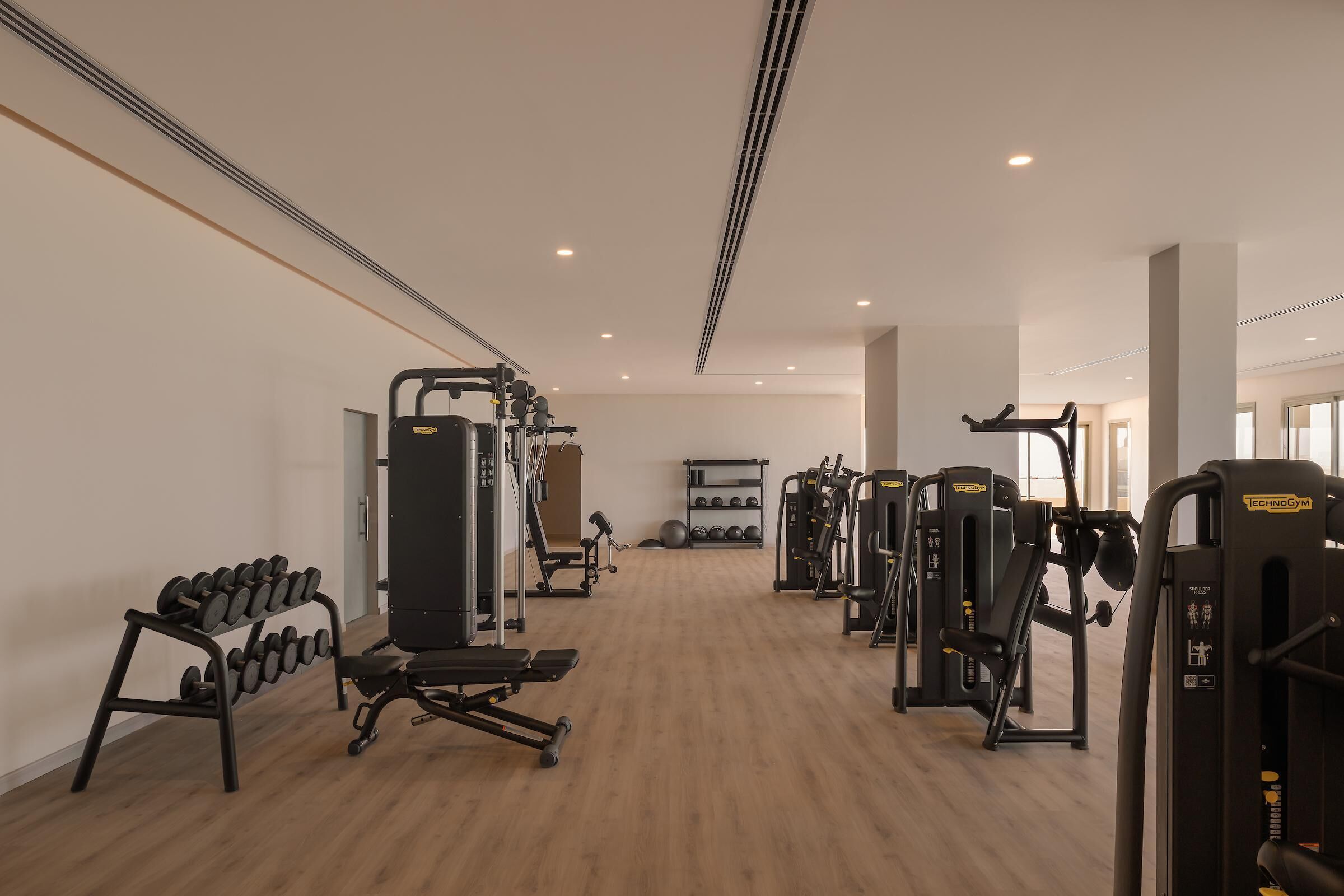 Un gimnasio con varios equipos de ejercicio, un estante de mancuernas y una banca.