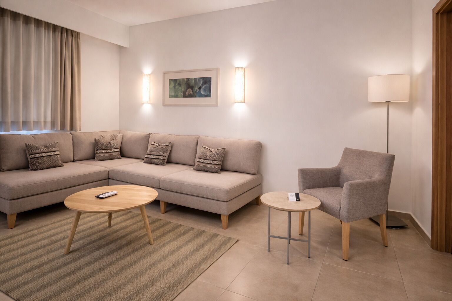 A modern living room with a sectional sofa, a round coffee table, a side table, a floor lamp, and a painting on the wall.