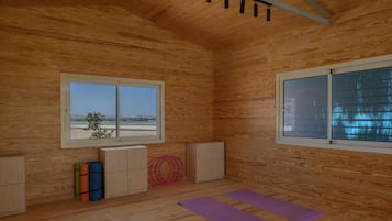 Una habitación con paredes de madera, dos ventanas, una lámpara de techo, un armario y colchonetas de yoga.