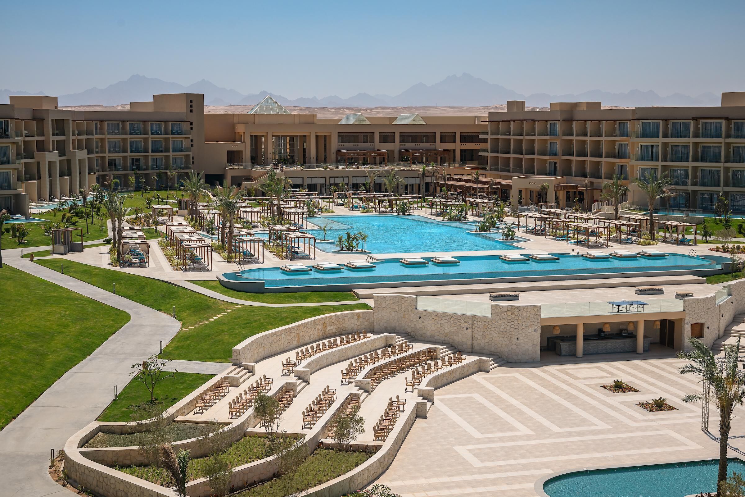 A hotel with a large pool, outdoor seating areas, and a view of mountains.
