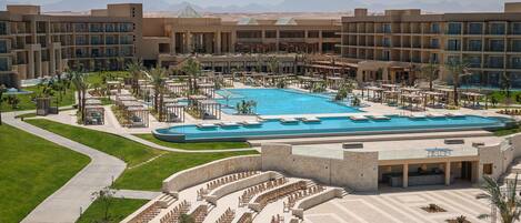 A hotel with a large pool, outdoor seating areas, and a view of mountains.