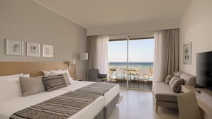 A hotel room with a large bed, a desk with a TV, a balcony with a pool view, and framed artwork on the wall.