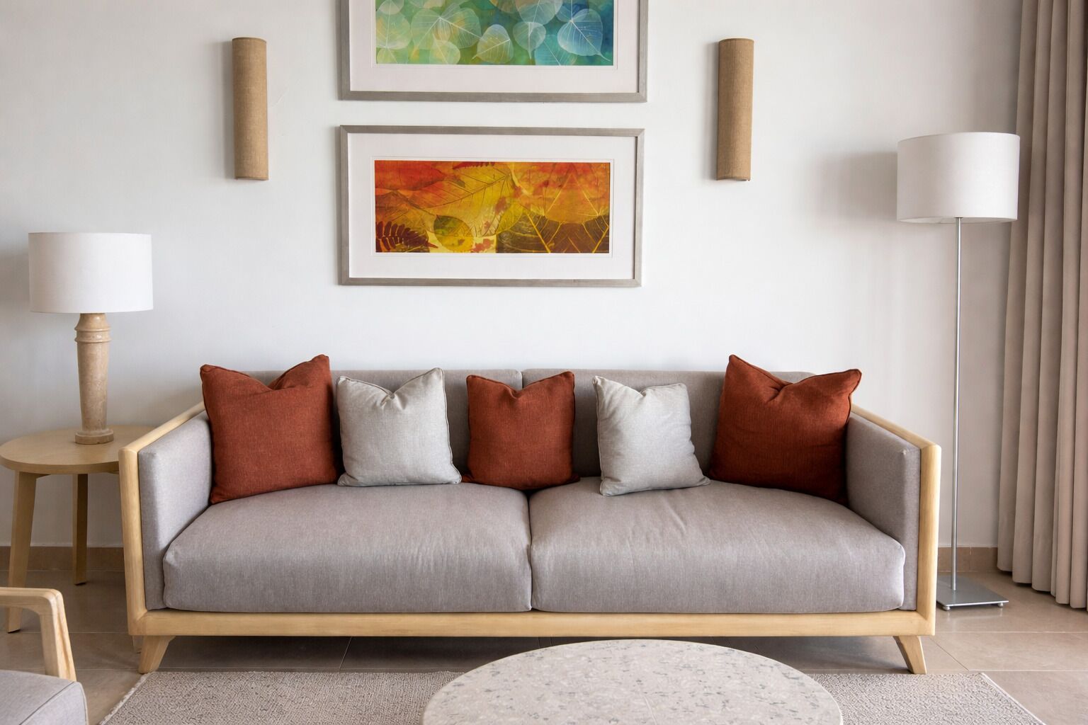 Uma sala de estar moderna com um sofá cinza, duas mesinhas de apoio e duas pinturas abstratas emolduradas na parede.