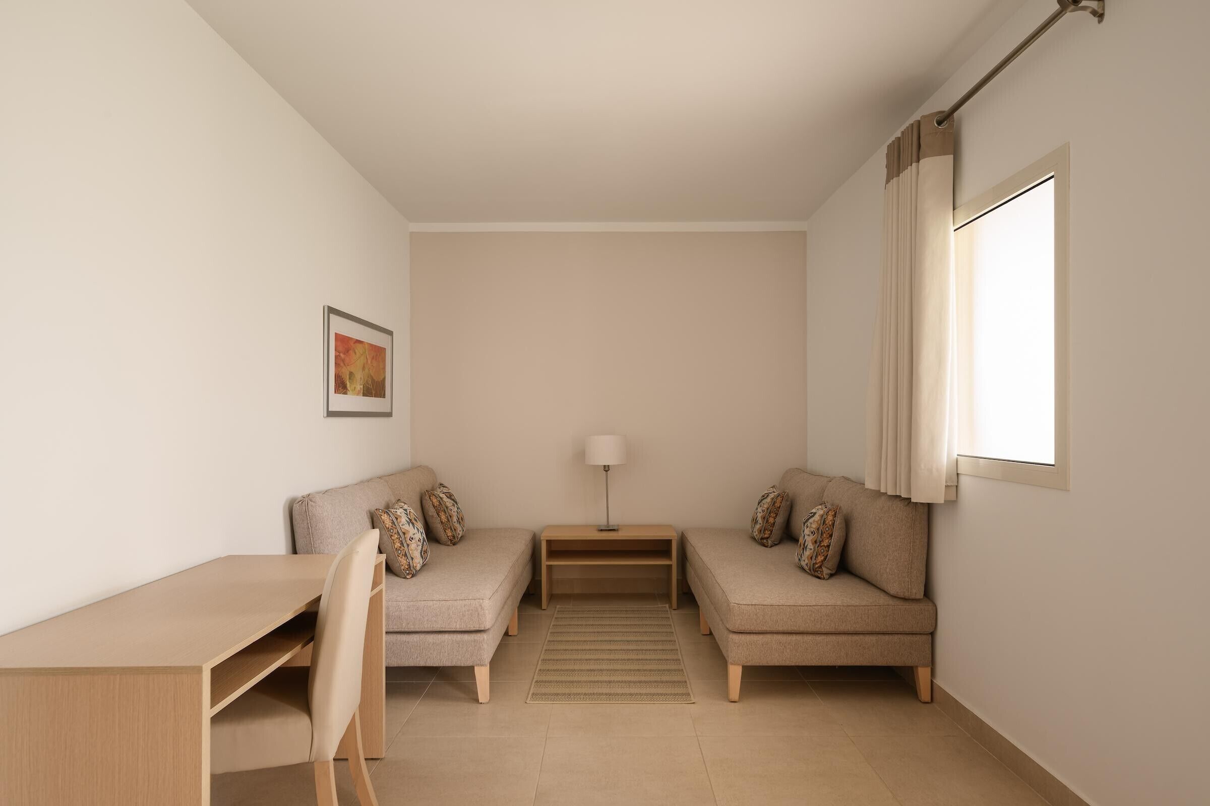 A minimalist room with two sofas, a small table, a lamp, and a single framed picture on the wall.