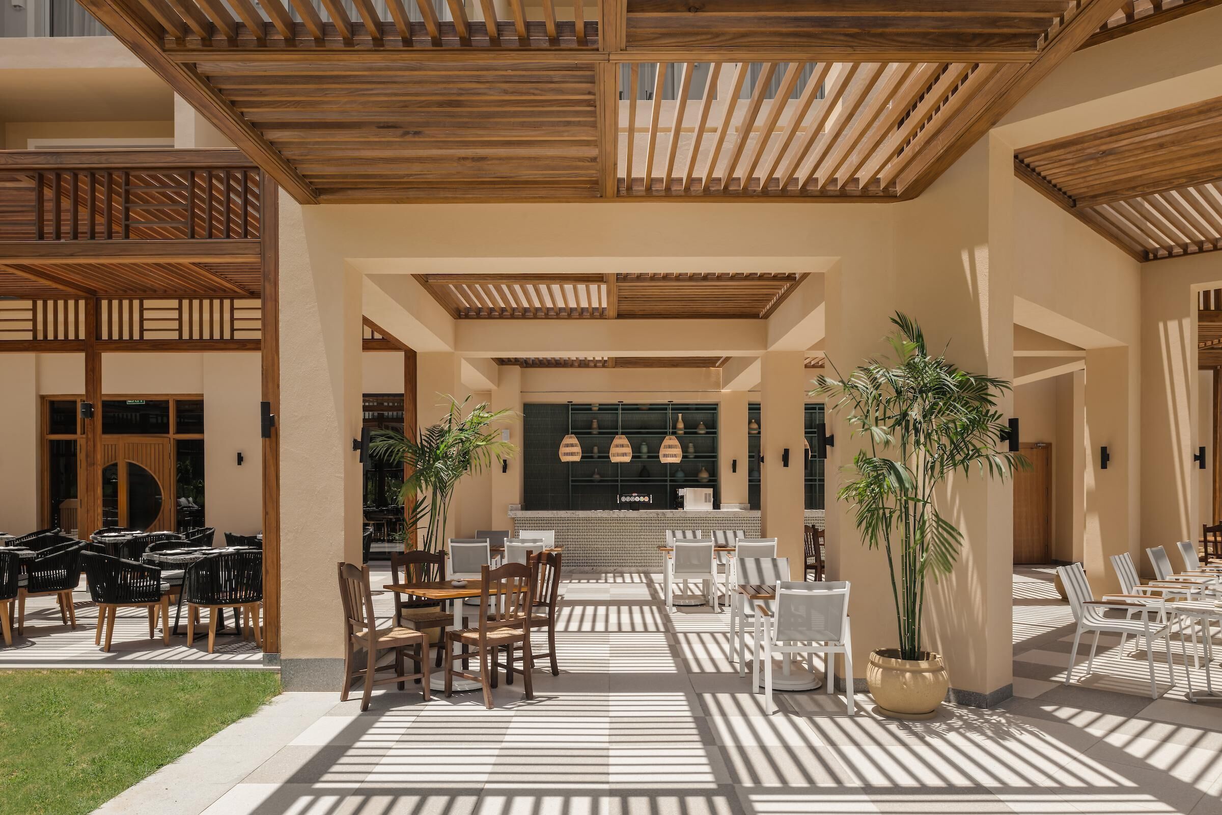 A covered outdoor seating area with tables and chairs, a central bar, and potted plants.