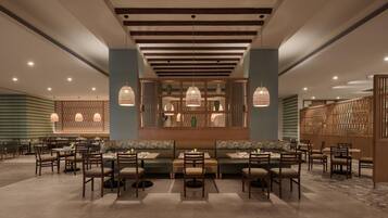 A restaurant with a central seating area, multiple tables, and hanging pendant lights.