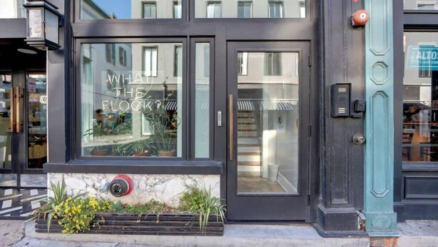 Un edificio con fachada de vidrio, una puerta con un letrero que dice “WHAT THE FLOOR?” y un hidrante debajo.