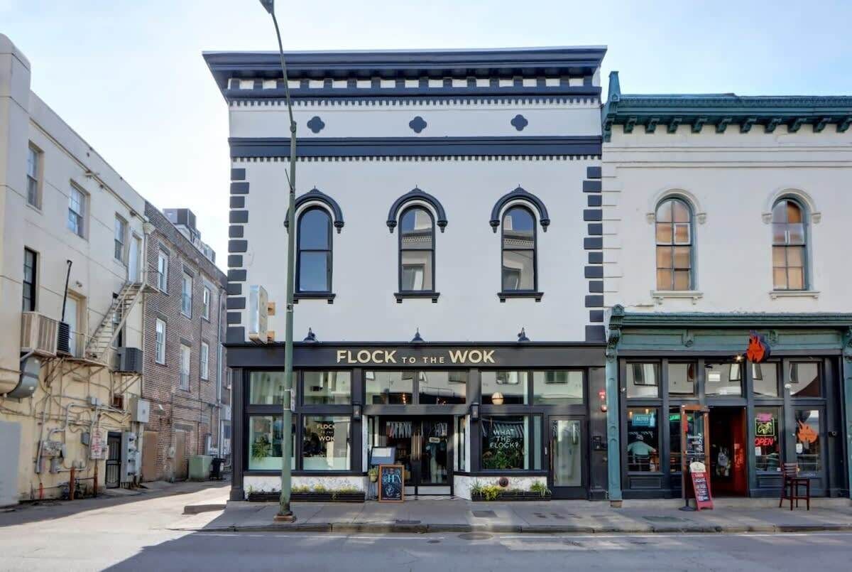 A building with a storefront named 'FLOCK TO THE WOK' featuring large windows, a flat facade, and a corner location.