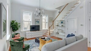 Una sala de estar moderna con una escalera, un televisor de pantalla plana, sillones verdes y un sofá gris.