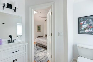 Une salle de bain moderne avec un lavabo blanc, un robinet noir et un miroir. On peut voir un tableau encadré au mur et des toilettes.