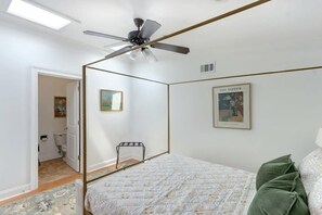 A bedroom with a bed, a ceiling fan, a framed picture, and a door leading to a bathroom.
