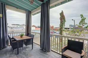 Ein Balkon mit Tisch und Stühlen, Blick auf eine Stadtlandschaft und eine hohe Pflanze mit Blüten.