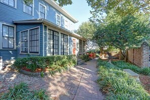 A two-story house with a brick pathway leading to a patio area. - Avery's Cottage @ Trustees' Garden | Walk 2 River! (Savannah)