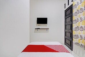 Simple, functional room with a single bed, flat-screen TV, and patterned curtain.
