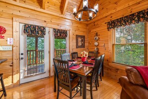 A wooden cabin interior with a dining table set for six, surrounded by chairs. - Log cabin convenient to Dollywood, Townsend, & National Park (Sevierville)