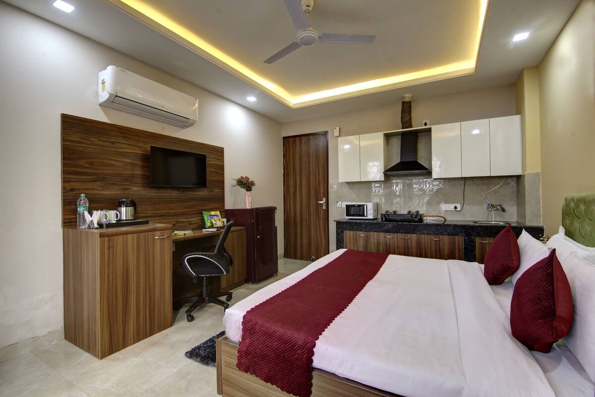 Une chambre d’hôtel moderne équipée d’un lit, d’un bureau, d’une chaise, d’un climatiseur, d’une télévision et d’une kitchenette.