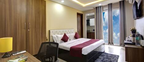 A hotel room with a bed, desk, chair, and a view of the sky through the window.