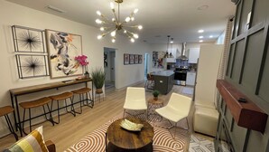 Una sala de estar moderna con comedor, una cocina al fondo y un ventanal grande.