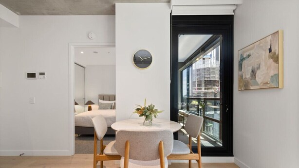 Ein modernes Wohnzimmer mit einem runden Esstisch, zwei Stühlen, einer Wanduhr und einem großen Fenster mit Blick auf die Stadt.