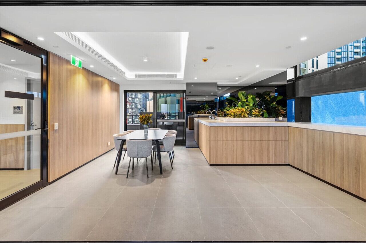 A modern hotel lobby with a reception desk, a seating area with a table and chairs, and a large window offering a view of the city.