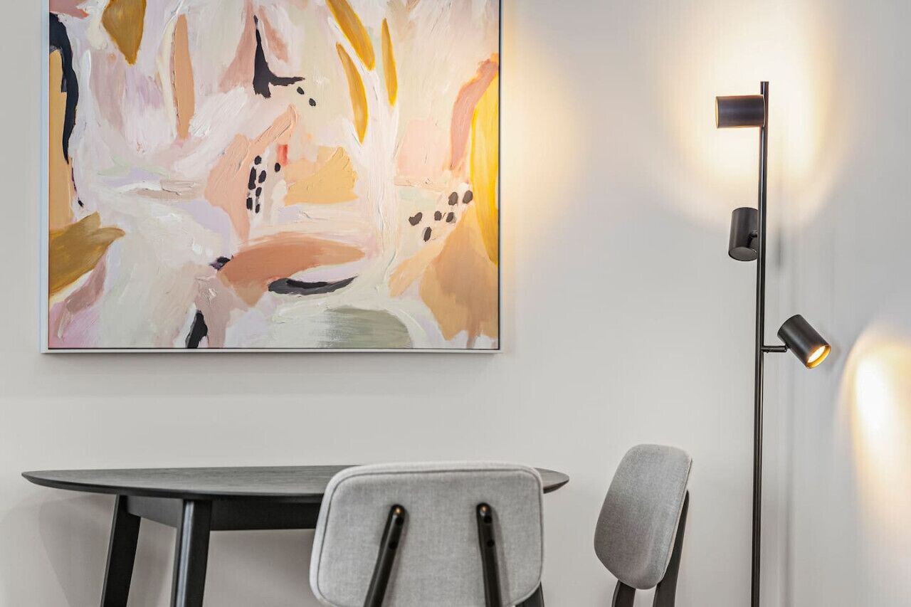 A modern dining area with a minimalist table and chairs, a contemporary floor lamp, and a large abstract painting on the wall.
