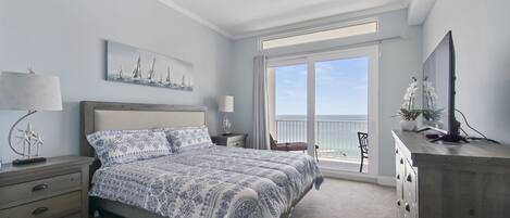 Un dormitorio con una cama grande, una mesita de noche, un aparador, un televisor, una ventana con vistas al mar y un cuadro en la pared.