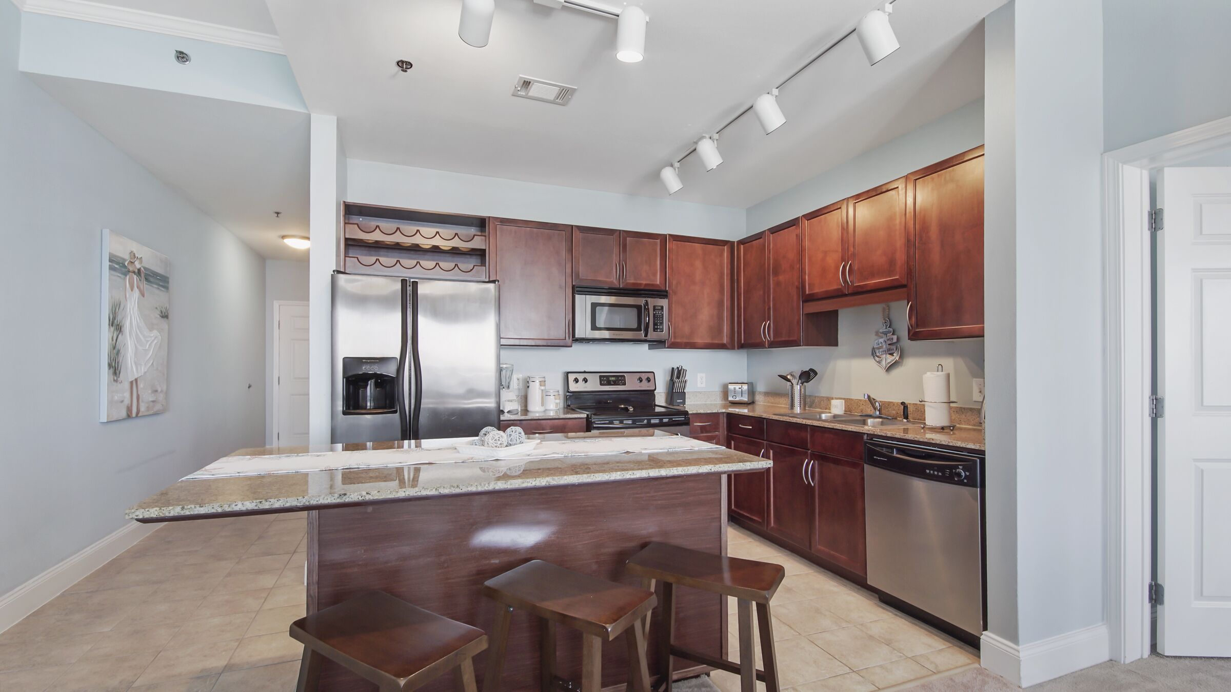 A modern kitchen with stainless steel appliances, wooden cabinets, and a central island with bar stools.