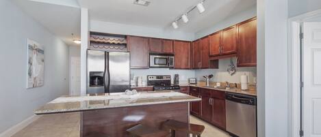 A modern kitchen with stainless steel appliances, wooden cabinets, and a central island with bar stools.