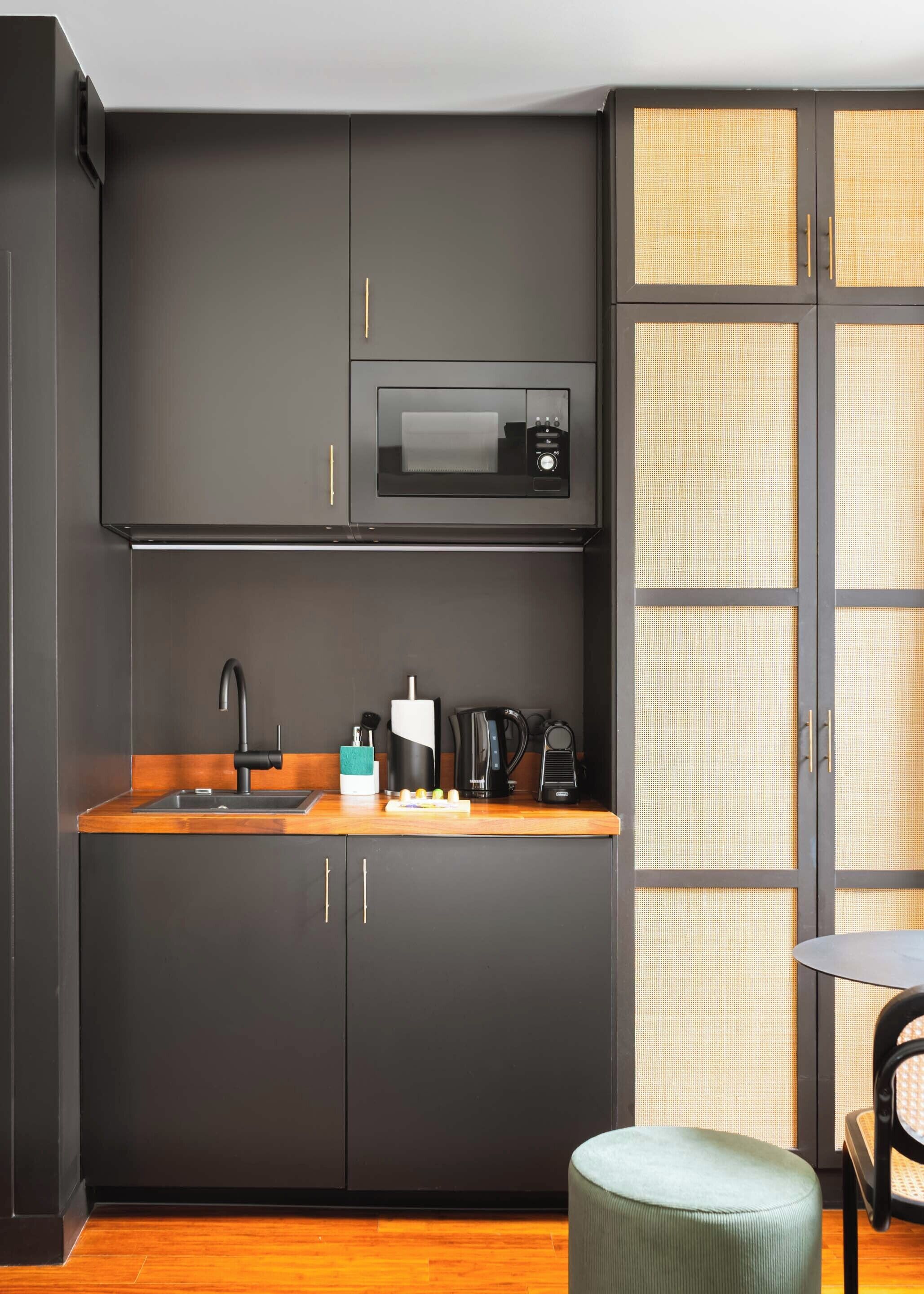 A compact kitchen with dark cabinetry, a built-in microwave, a sink, and a small dining area with a round table and a single chair.