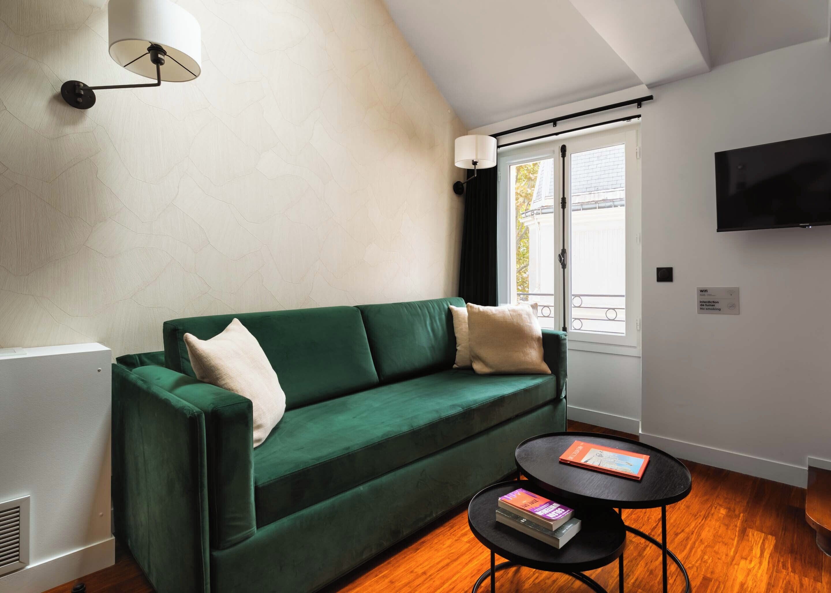 Un salon moderne avec un canapé vert, une table basse ronde noire et un téléviseur à écran plat fixé au mur.